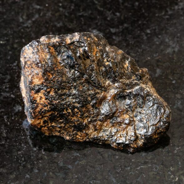 macro shooting of natural rock specimen - rough Cassiterite (Tin ore) stone on black granite background from Pravourmiyskoe deposit in Khabarovsk Krai, Russia