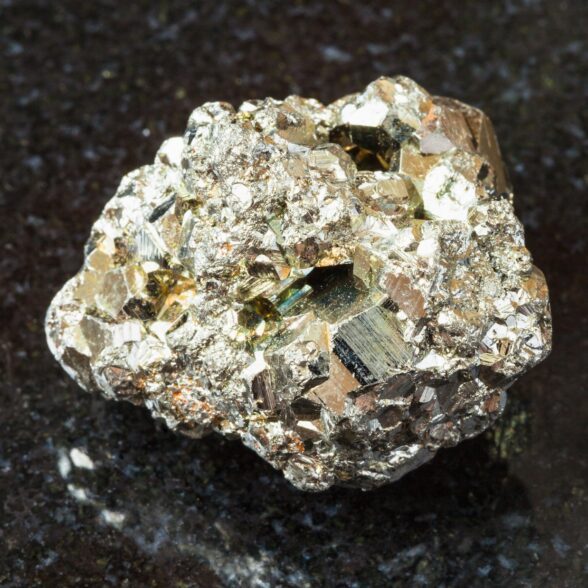 macro shooting of natural rock specimen - rough iron pyrite (fool's gold) stone on black granite background